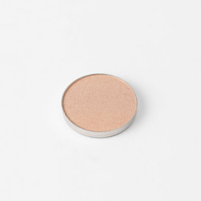 Pressed eyeshadow pan with warm peach shimmer finish, round compact.