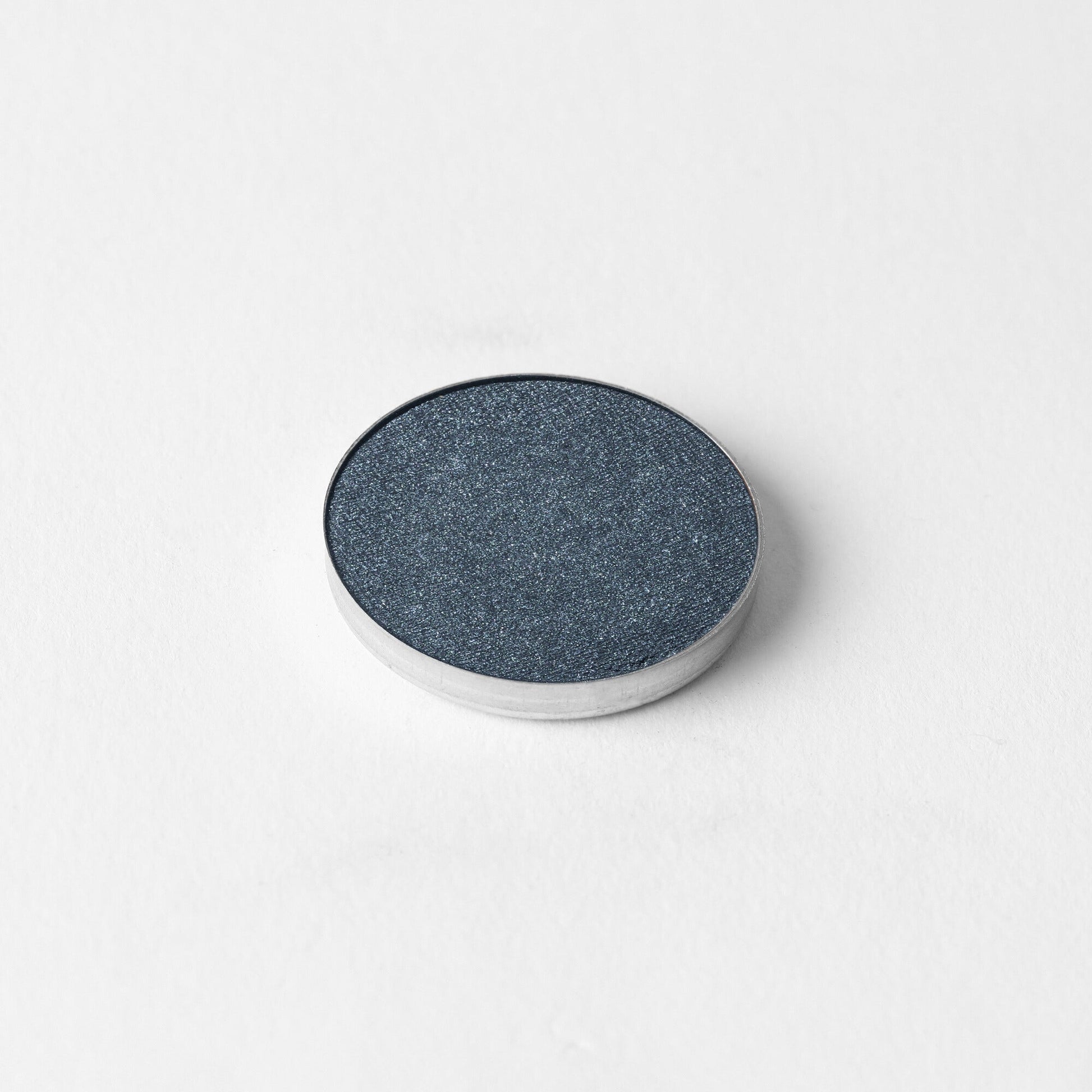Pressed eyeshadow pan, dark slate blue shimmer in a round compact.