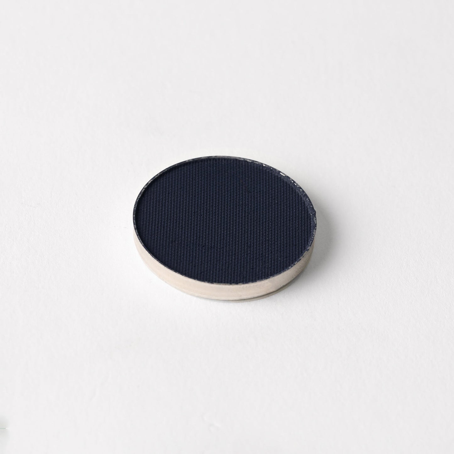 Matte pressed eyeshadow compact, deep navy-blue pan with textured surface
