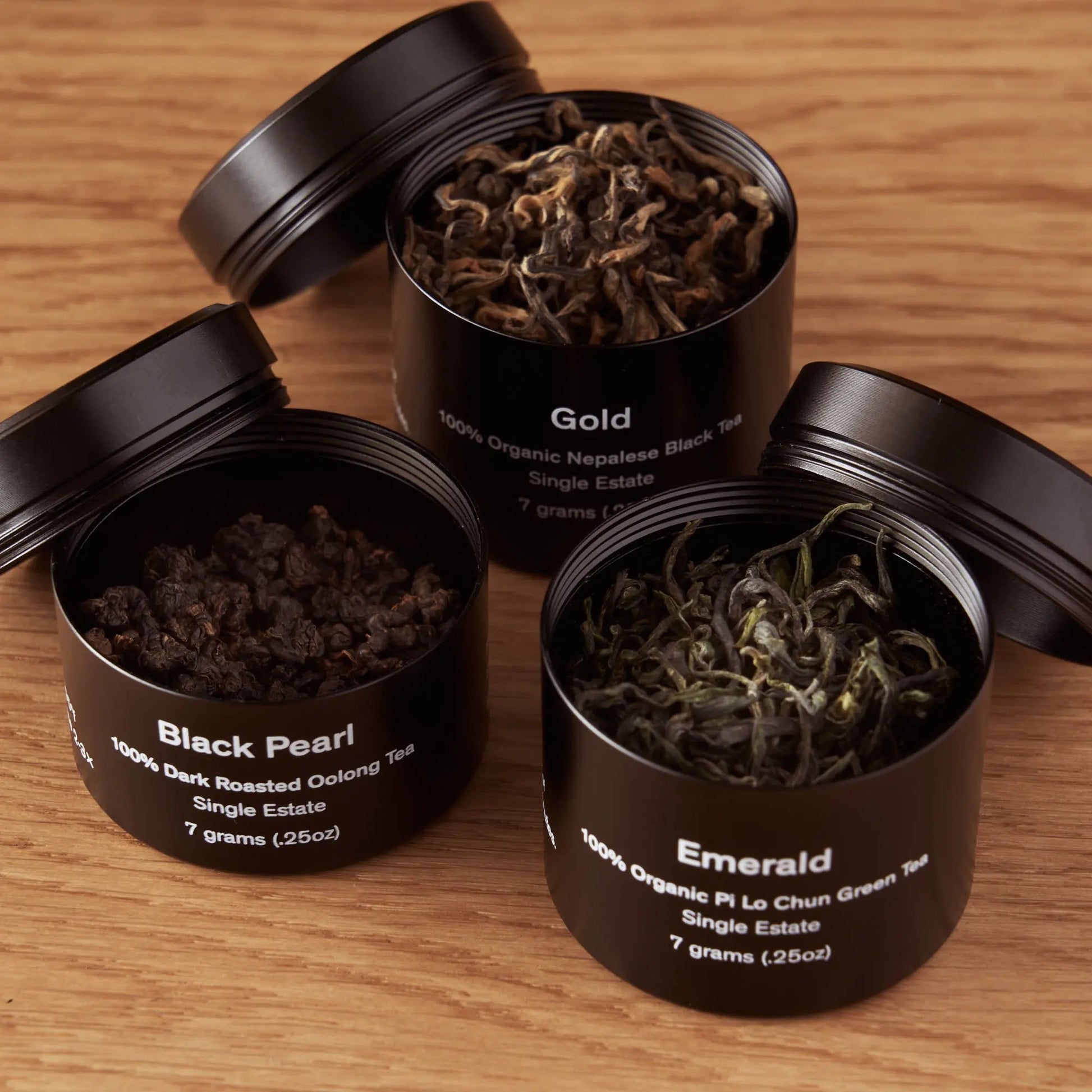 Three open tea mini tins with loose leaves: Black Pearl, Gold, Emerald.