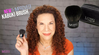 Kabuki makeup brush held by hand, black bristles with Mommy Makeup logo