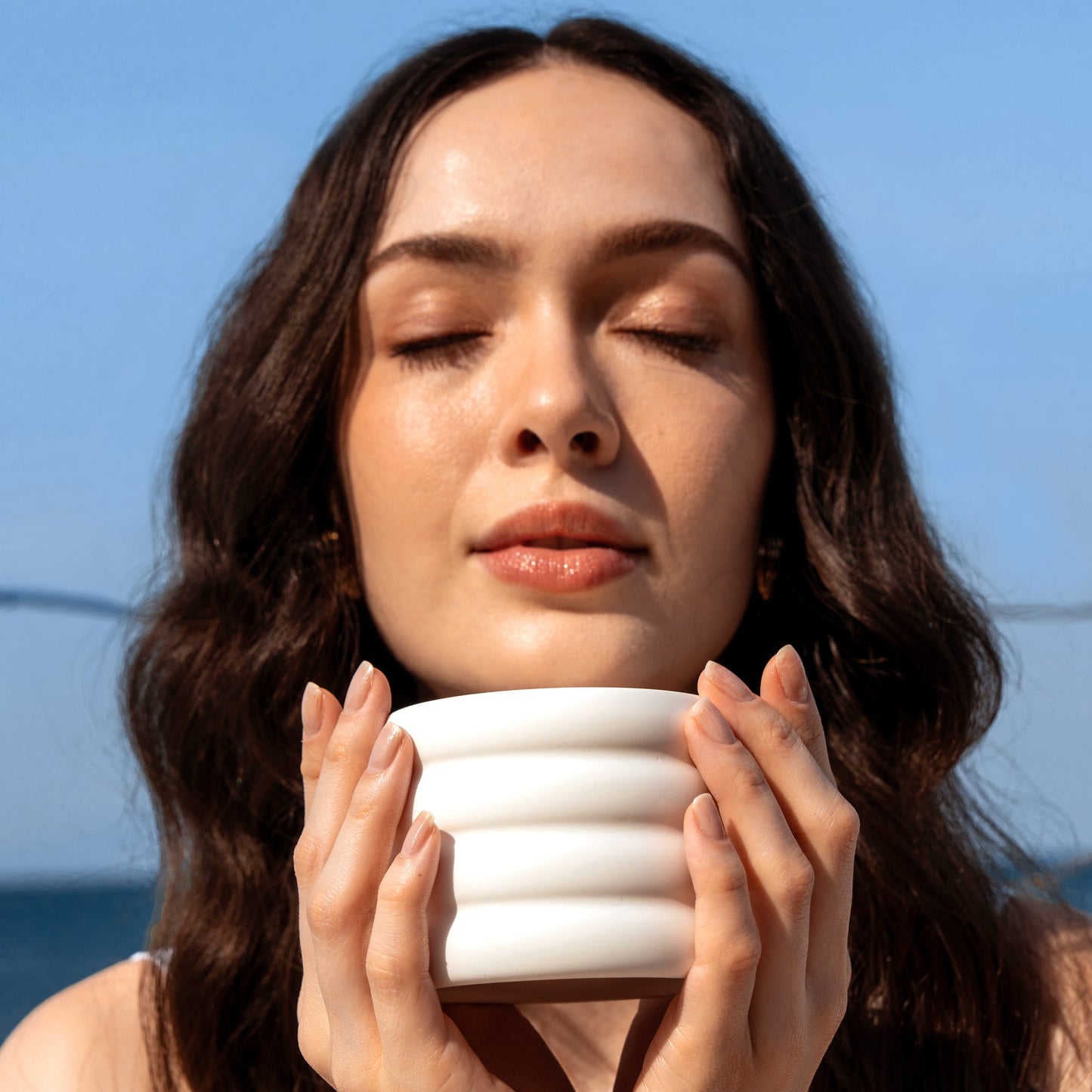 White ceramic soy wax candle cup held in hands with small flame