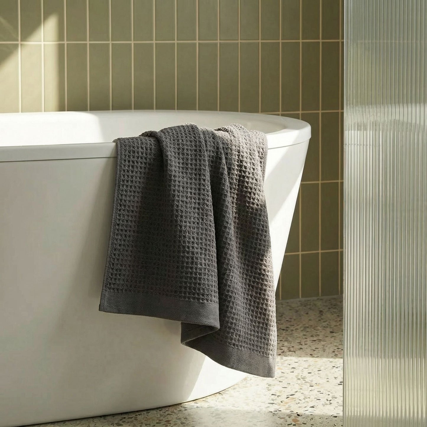 Charcoal waffle weave towel hanging from a bathtub edge, textured square pattern