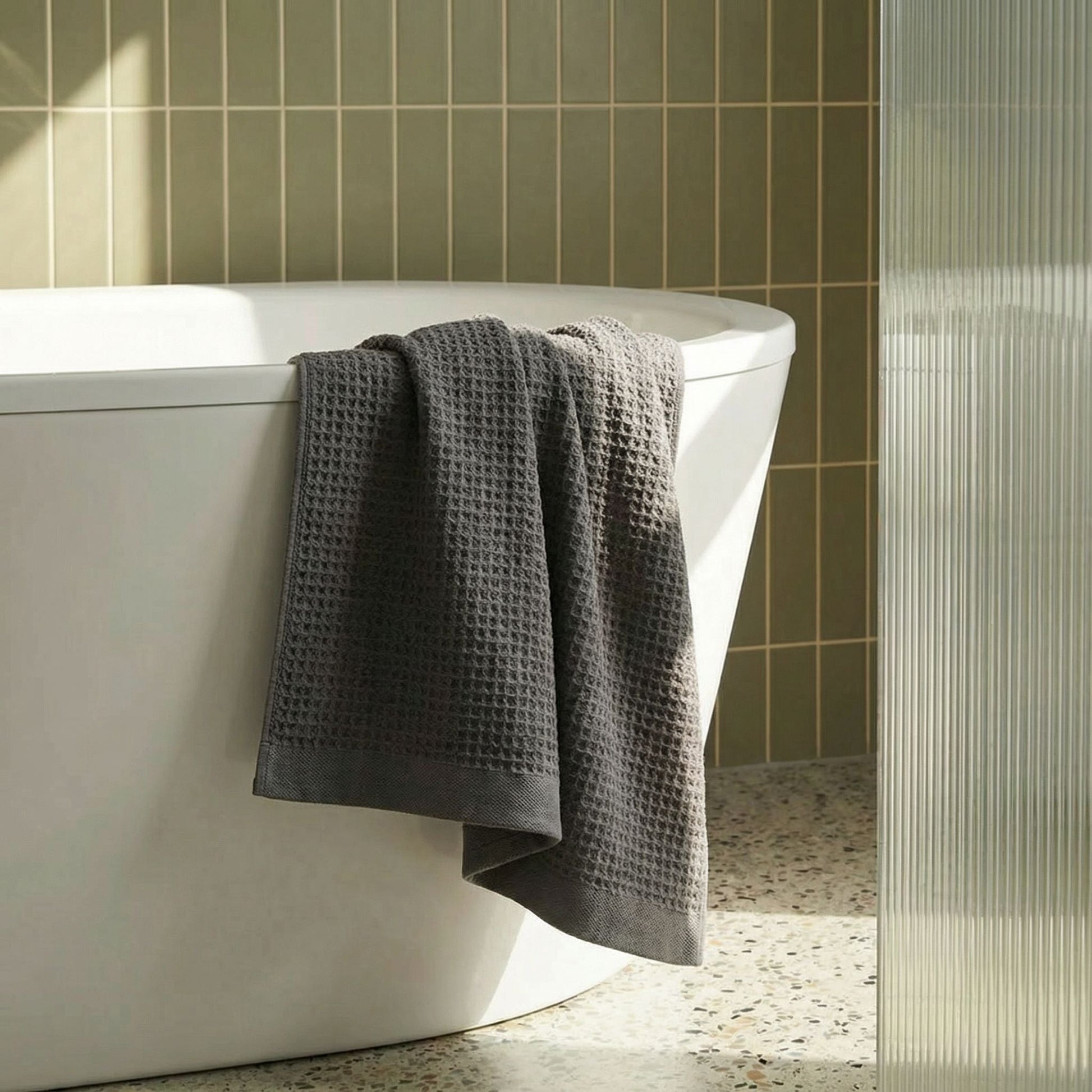 Charcoal waffle weave towel hanging from a bathtub edge, textured square pattern