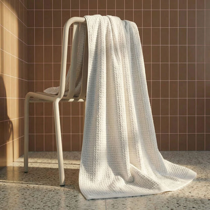 White waffle cotton bath towel hanging over a rack, showing textured weave.