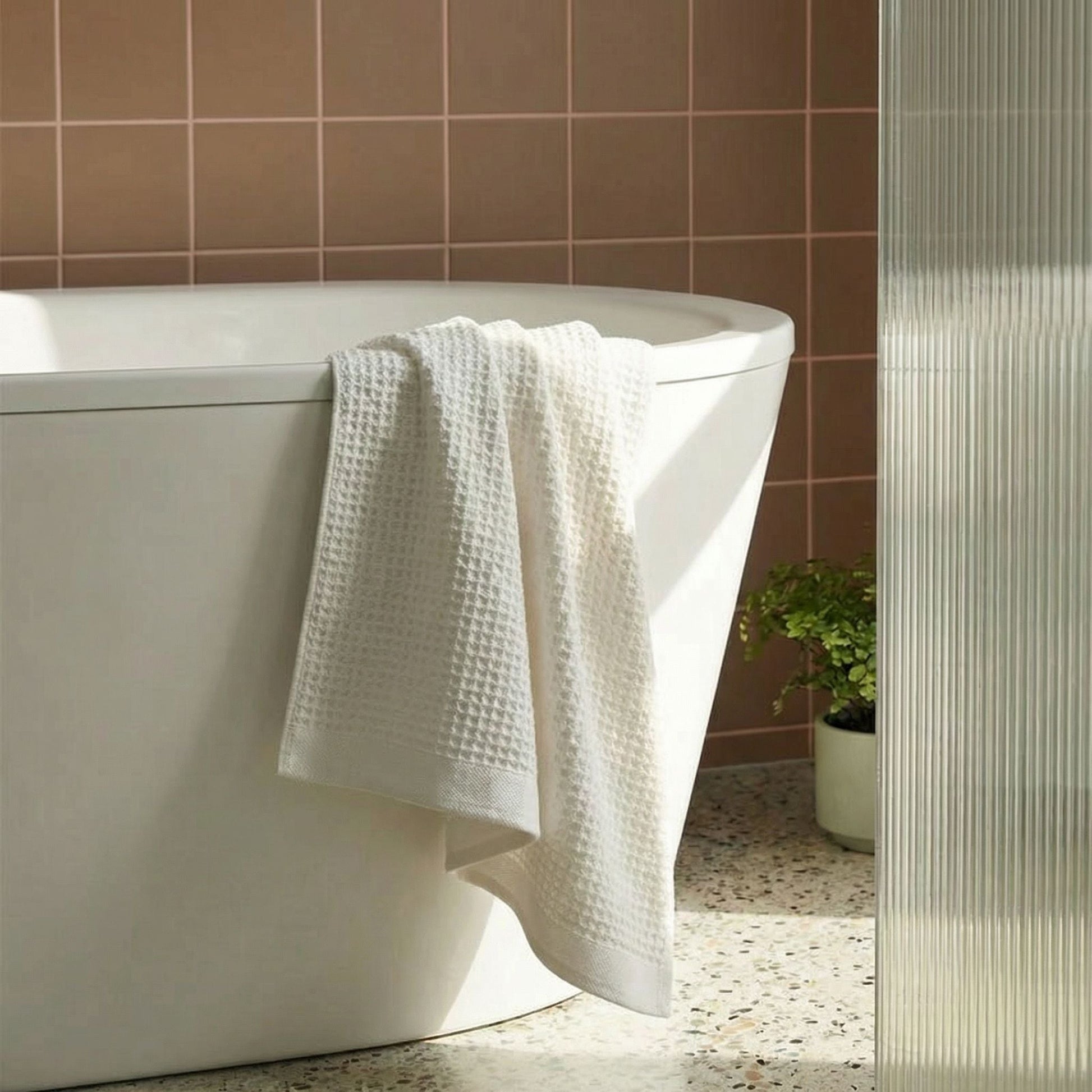 White waffle cotton towels draped over a bathtub edge, textured waffle surface.