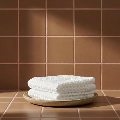 White waffle cotton towel folded on a small plate, textured waffle weave visible.