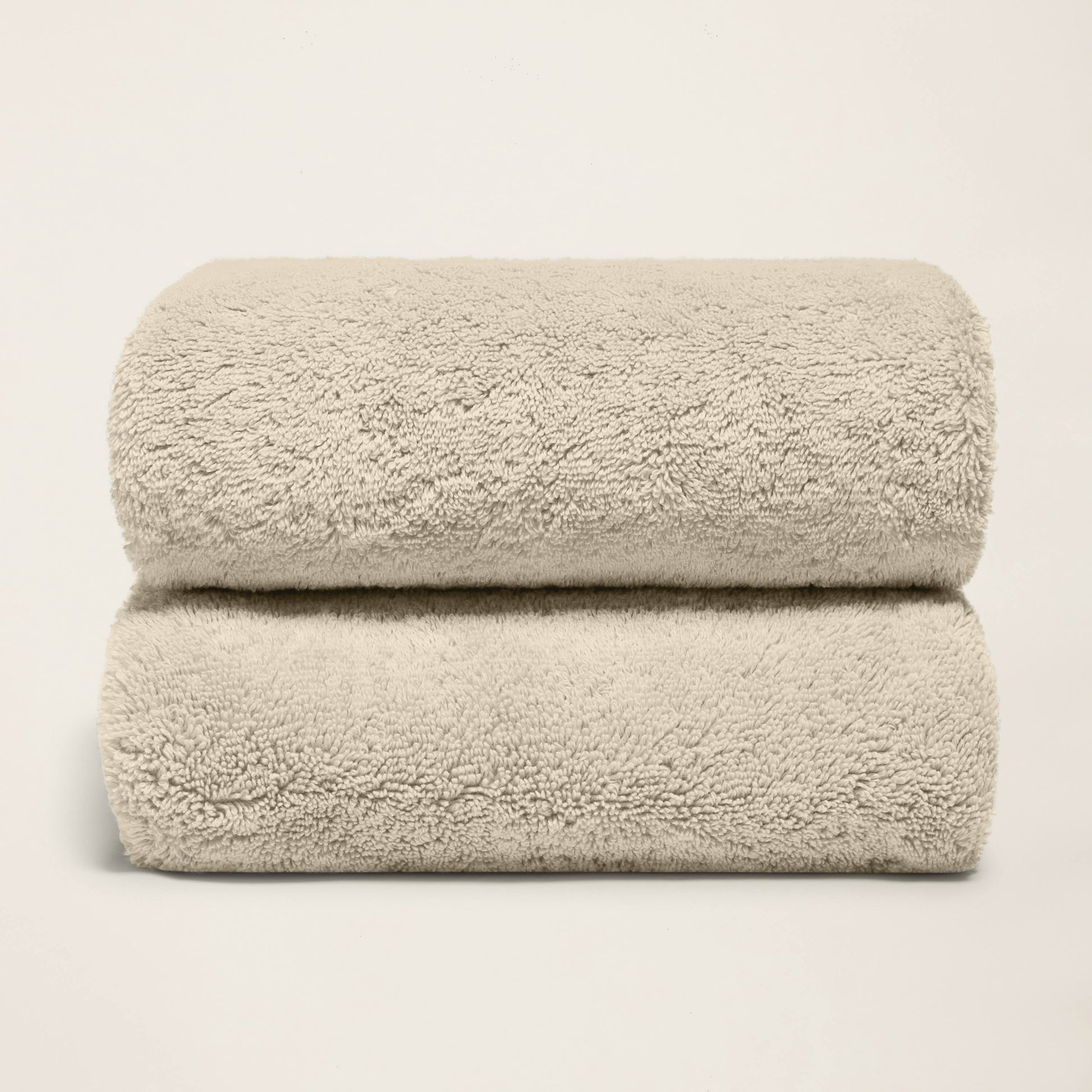 Stack of folded plush bath towels, light sand, terry loop pile.