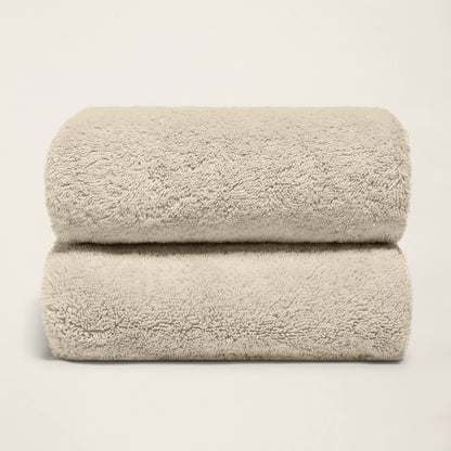 Stack of folded plush bath towels, light sand, terry loop pile.
