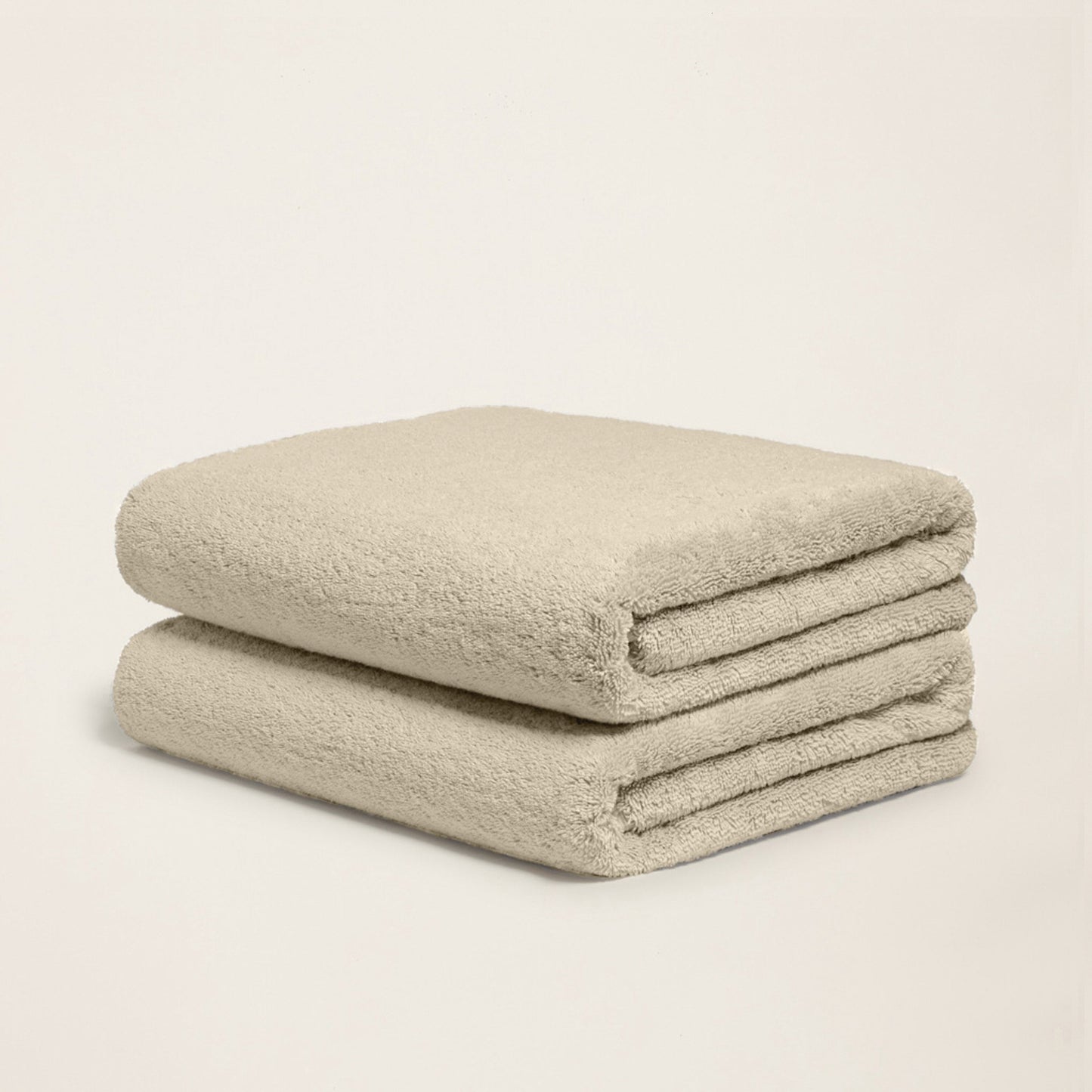 Two folded plush towels, light sand, soft terry texture, rolled edge view.