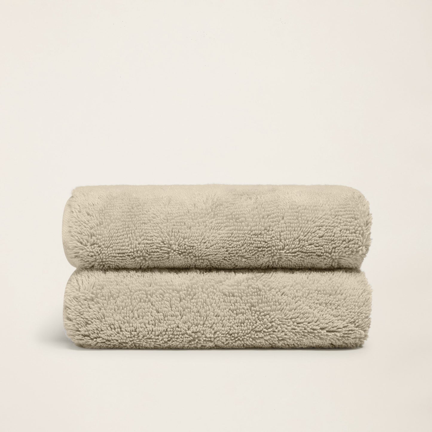 Stacked plush bath towels, light sand, thick terry loop pile.