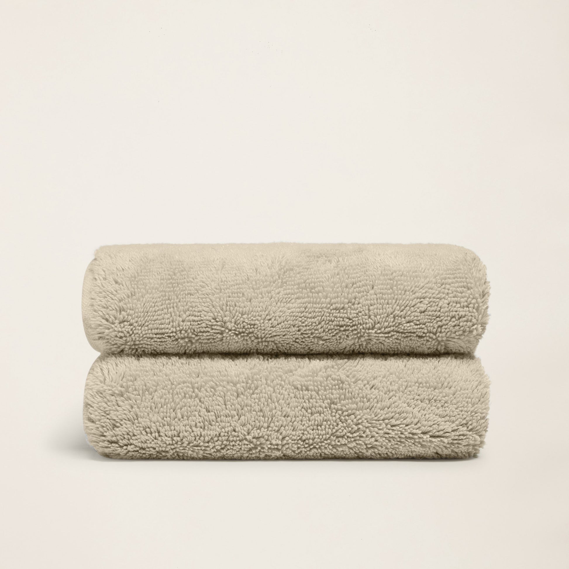 Stacked plush bath towels, light sand, thick terry loop pile.