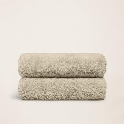 Stacked plush bath towels, light sand, thick terry loop pile.