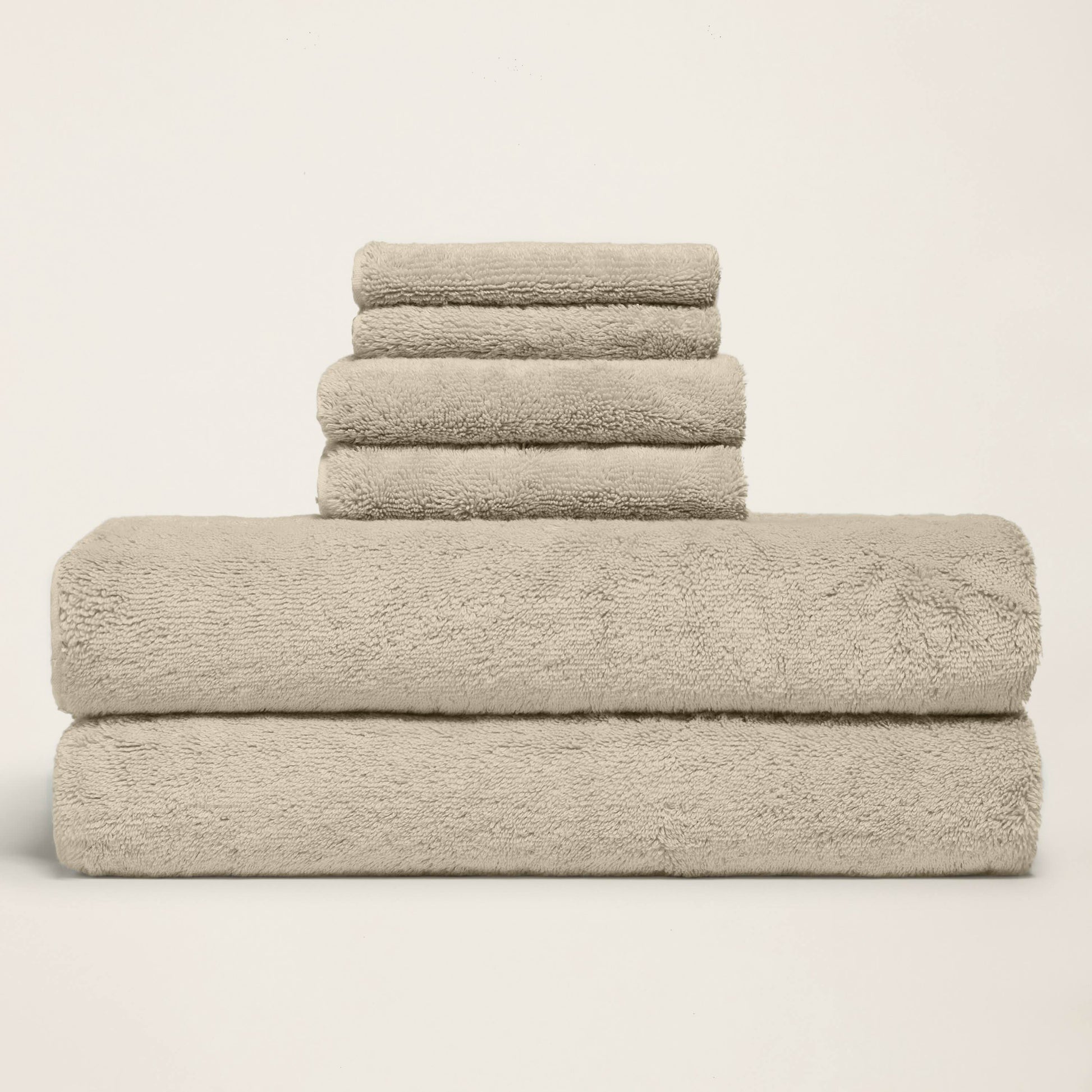 Folded towel set with one long towel stacked under three, light sand terry.