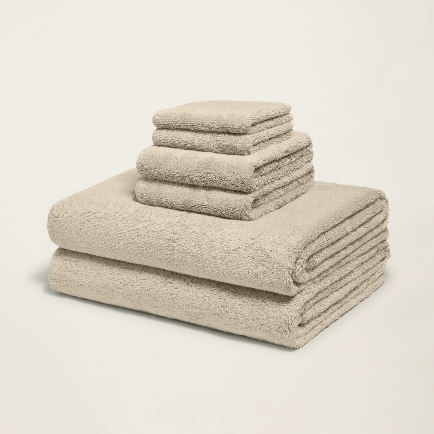 Stacked plush towels, light sand, thick terry loop pile, corner folded.