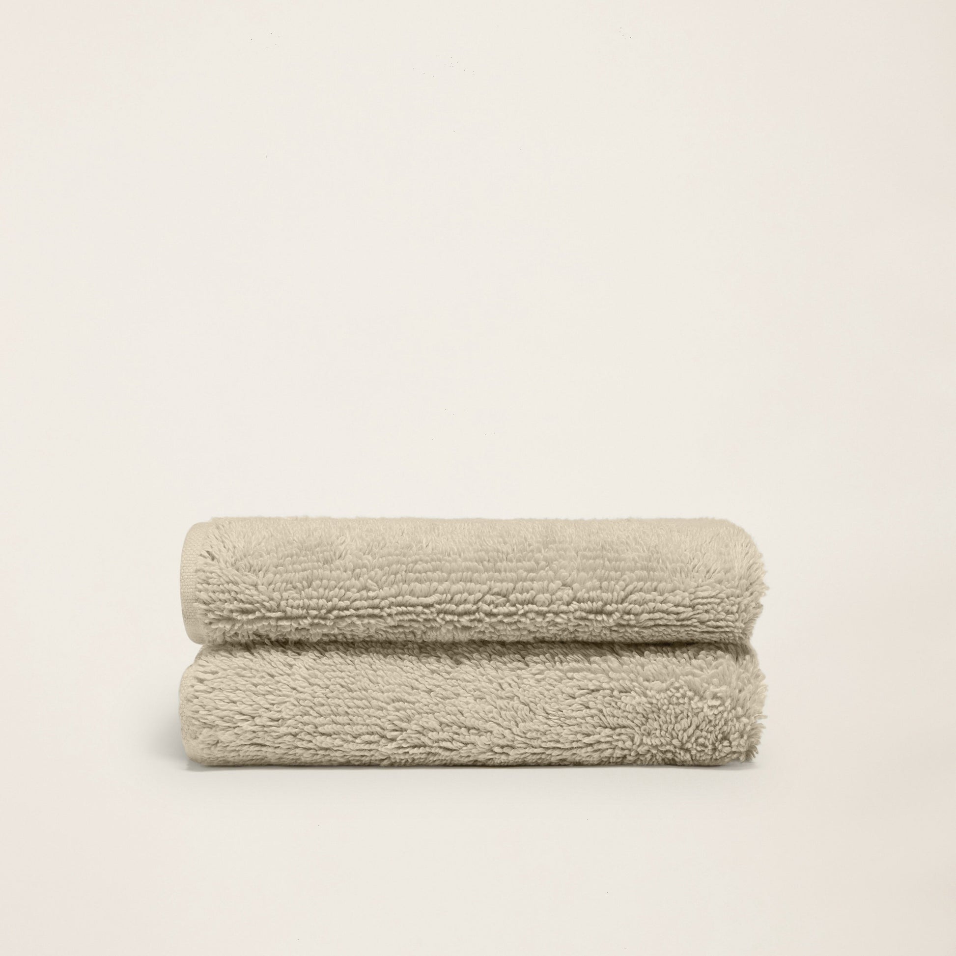 Pair of folded plush towels, light sand, dense terry loop pile.