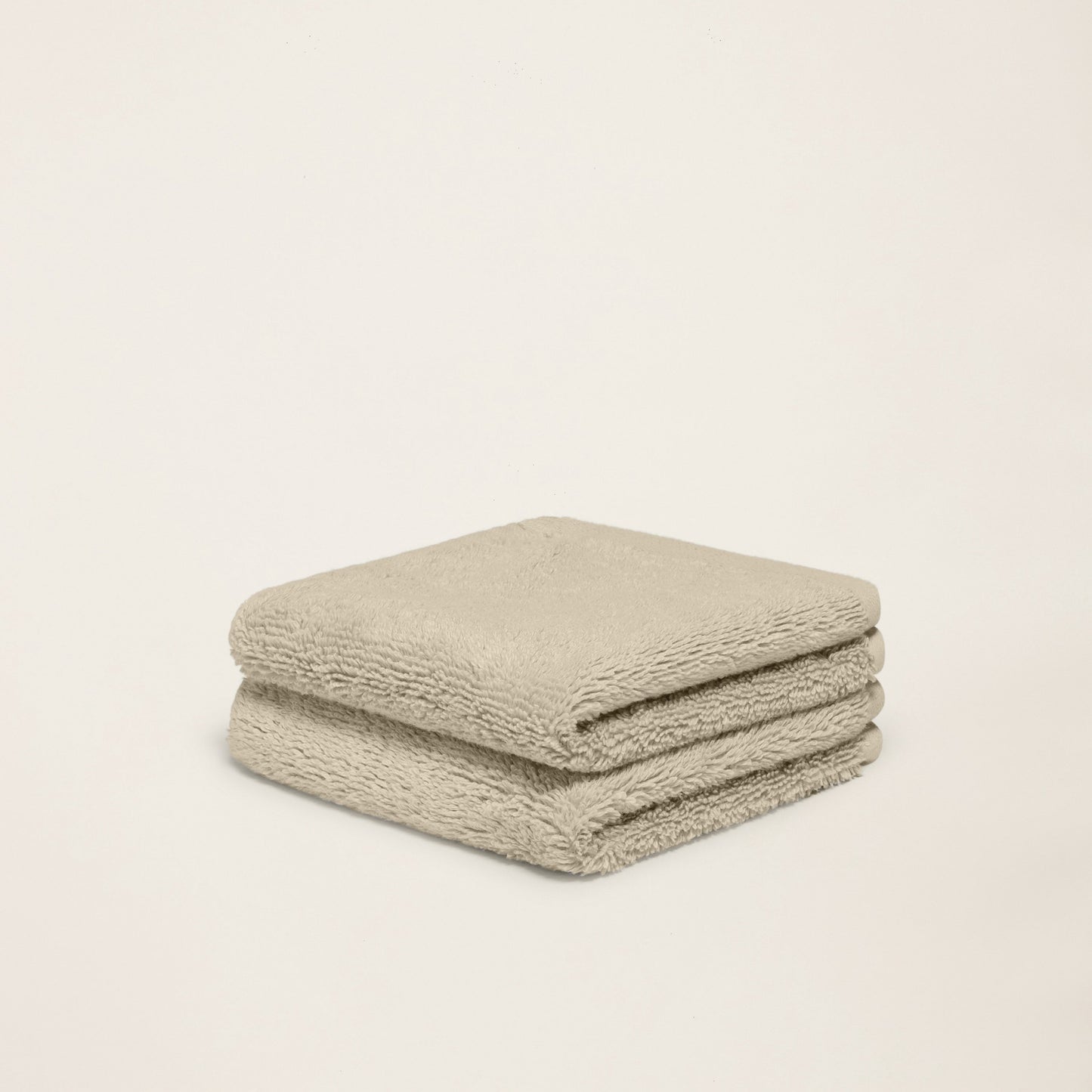 Folded plush towel, light sand, thick terry loop pile, neatly stacked.