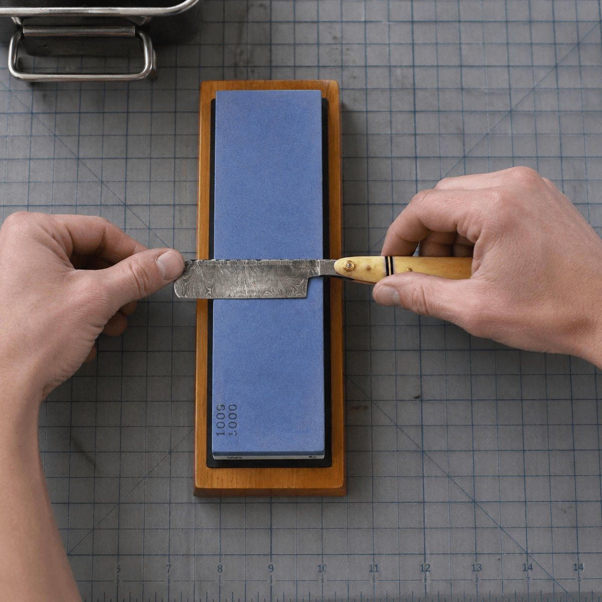 Sharpening stone in wooden holder with 1000/6000 grit, knife being sharpened