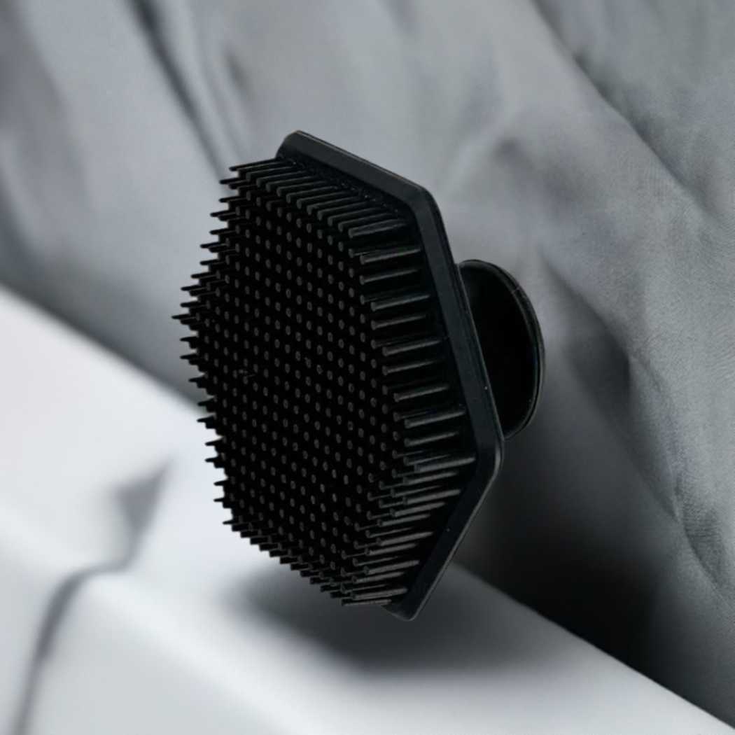 Black silicone face scrubber resting on a light fabric surface; bristle pad visible
