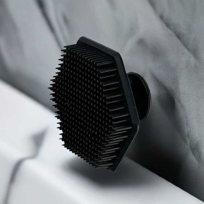 Black silicone face scrubber resting on a light fabric surface; bristle pad visible