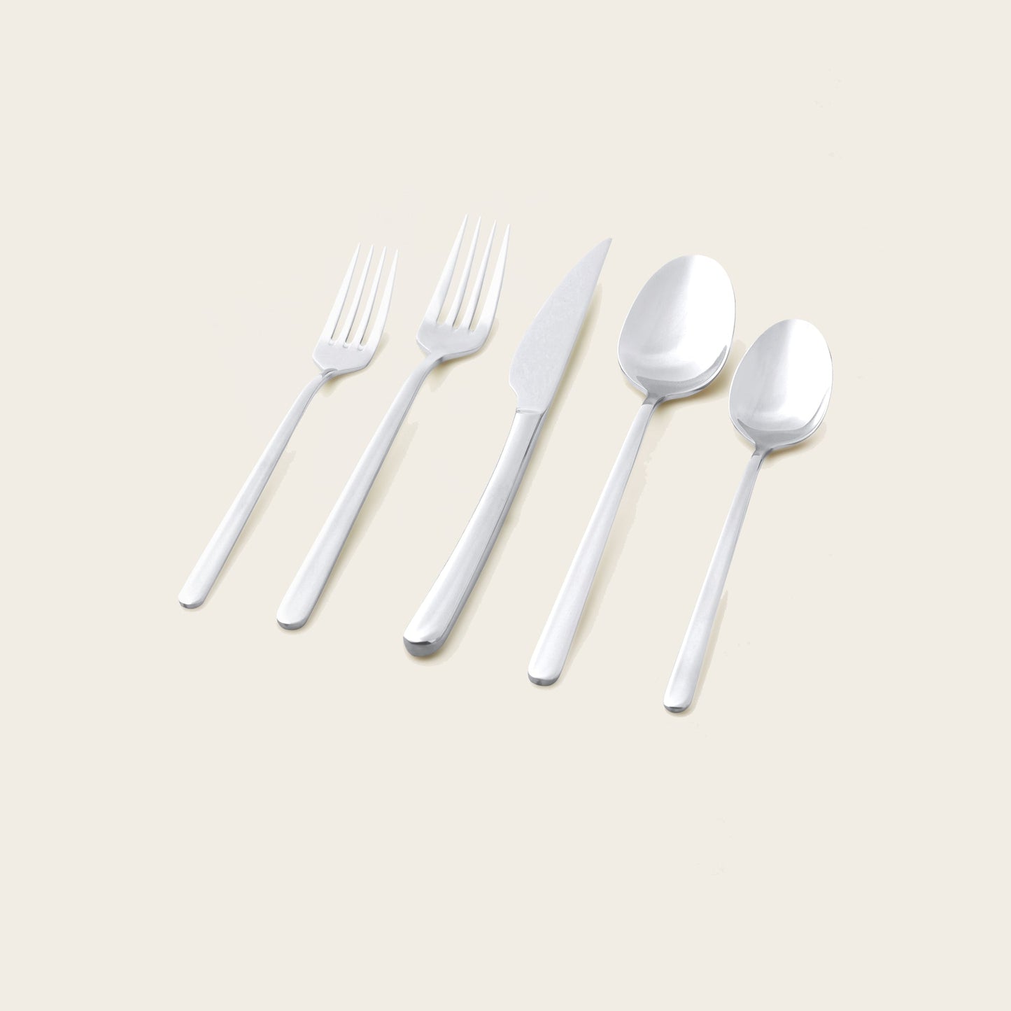 Silver flatware set pieces laid out: forks, knives, and spoons on a light surface
