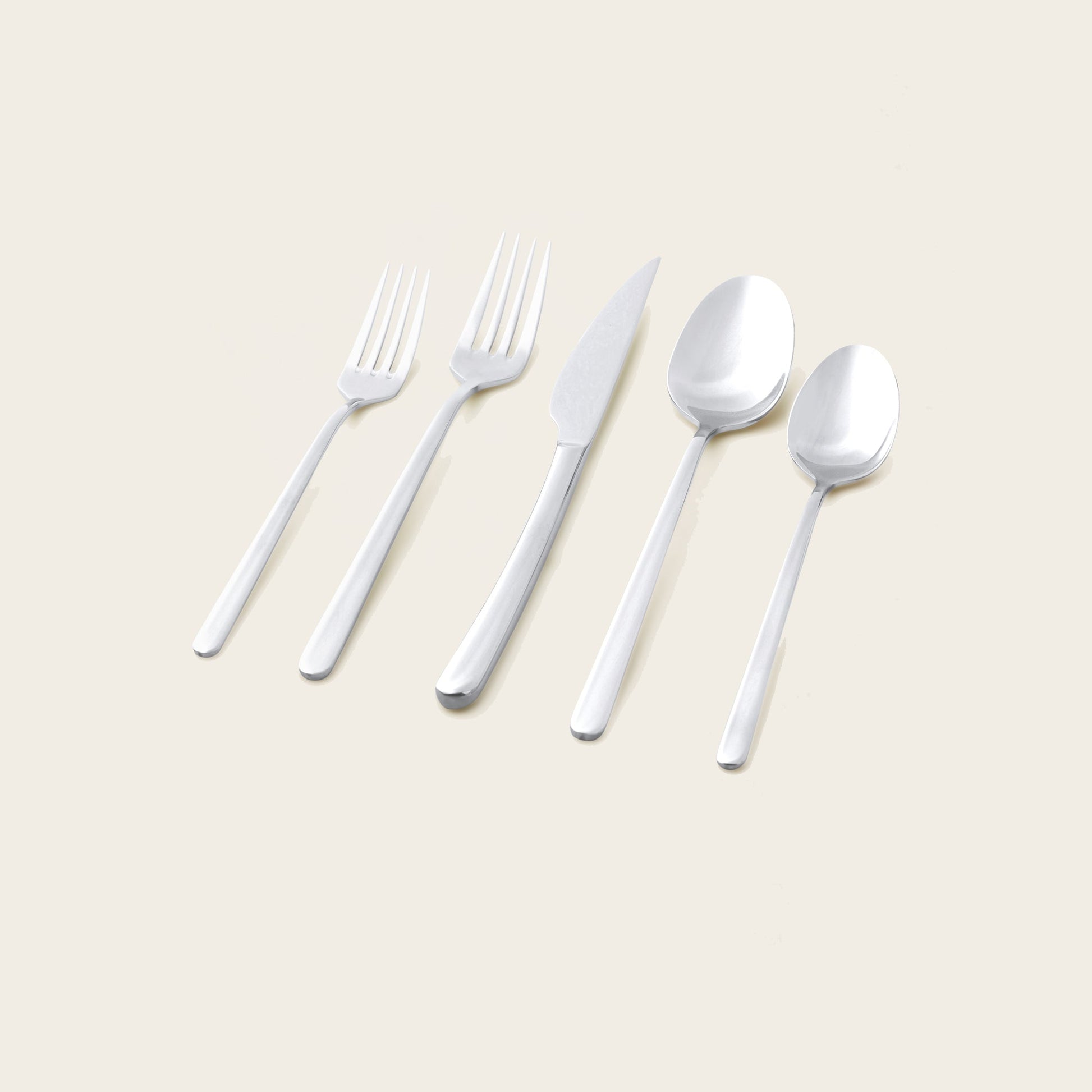 Silver flatware set pieces laid out: forks, knives, and spoons on a light surface