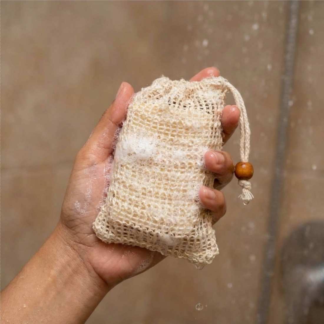 Soap saver bag, beige mesh pouch holding a bar of soap, drawstring with bead