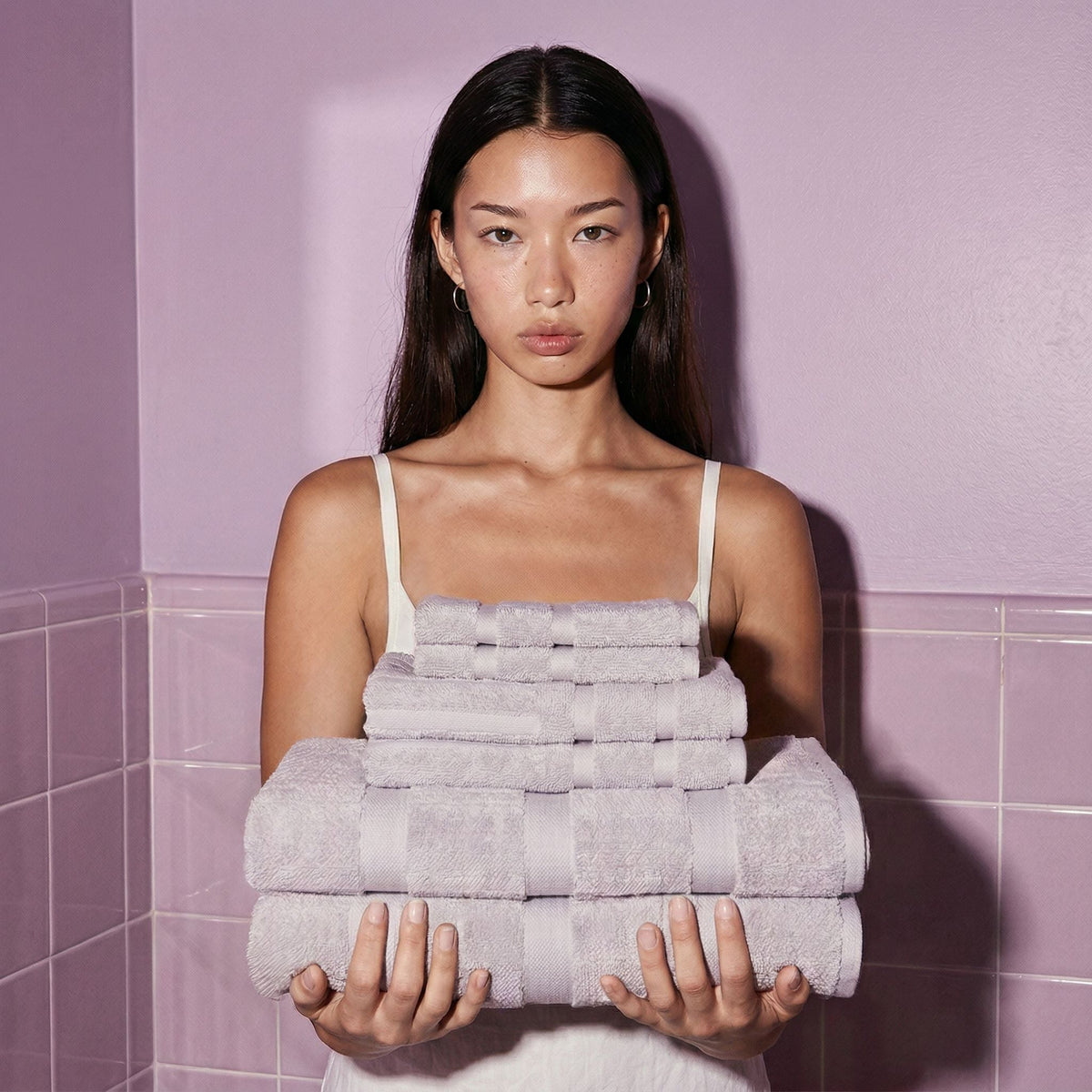Lilac cotton towels stacked and held against tiled wall