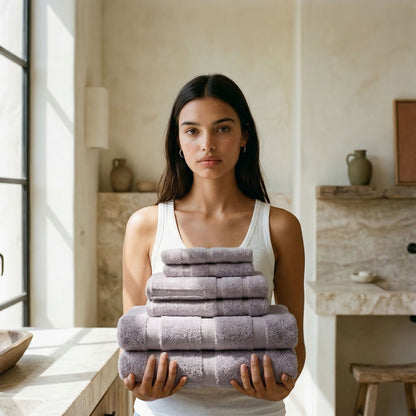 Lilac cotton towels folded into a stack, held by a person in a bathroom setting.