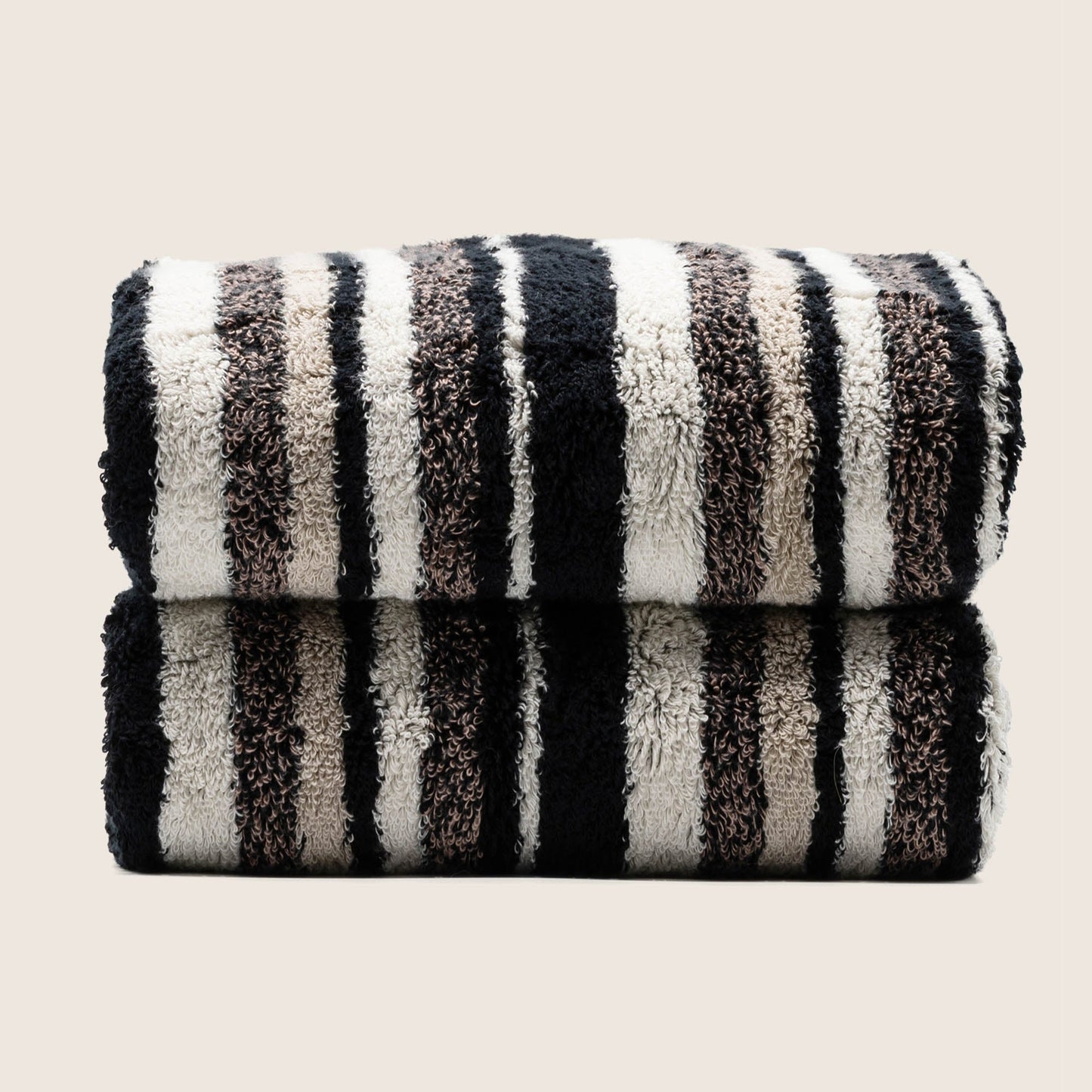 Two folded plush towels with dark and light vertical stripe pattern, tightly stacked.