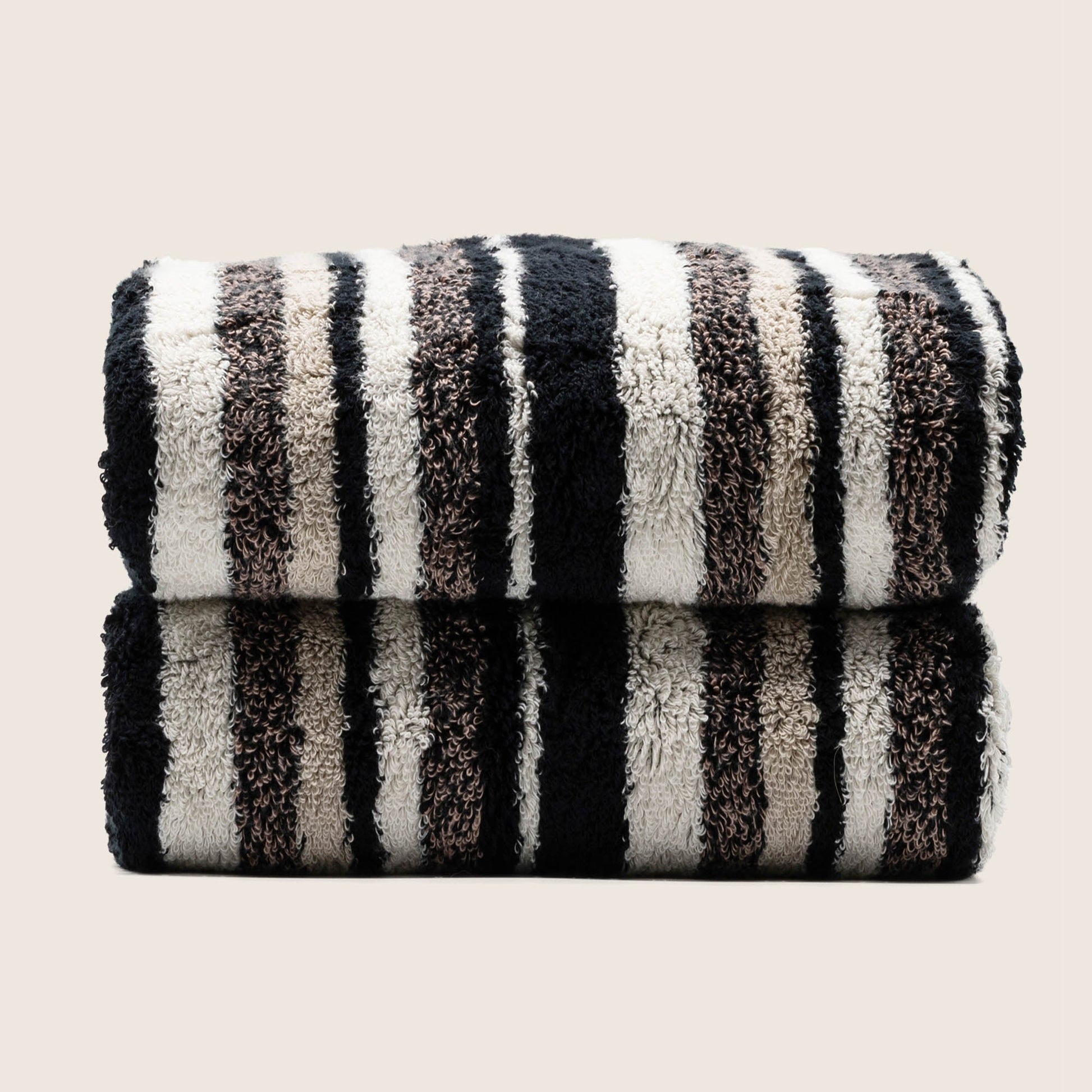 Two folded plush towels with dark and light vertical stripe pattern, tightly stacked.
