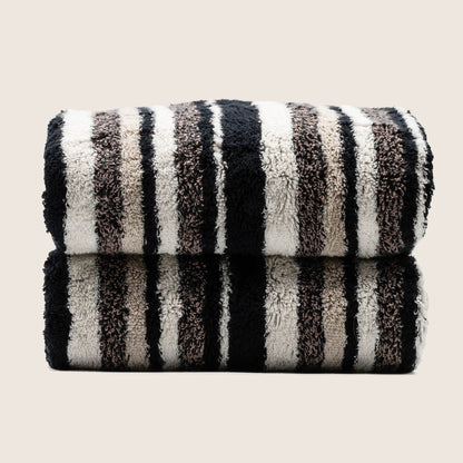 Two folded plush towels with dark and light vertical stripe pattern, tightly stacked.