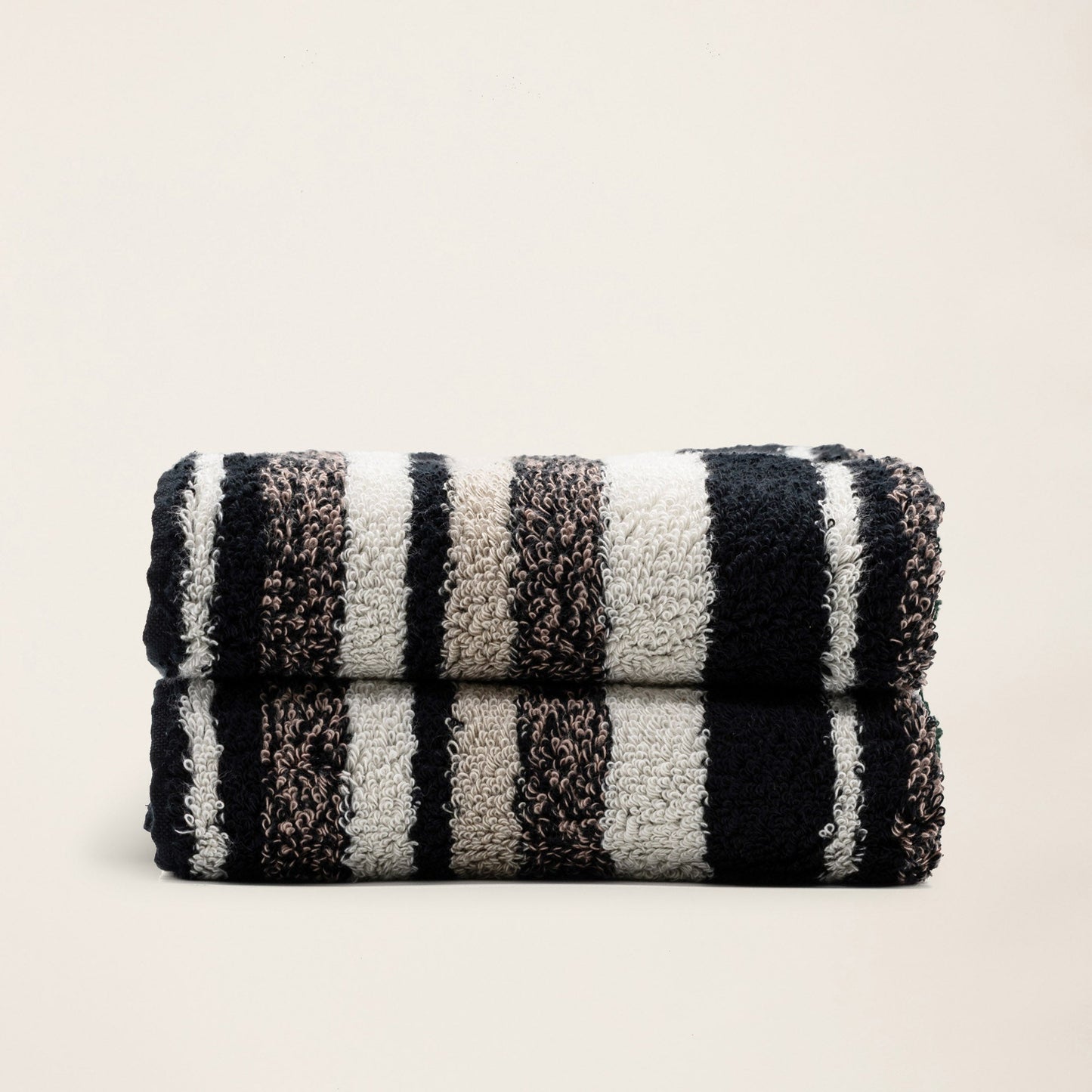 Rolled plush towels with dark and light vertical stripe pattern, neatly folded in a stack.