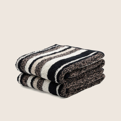 Folded striped towel with bold dark and light bands, plush texture visible at the edge.