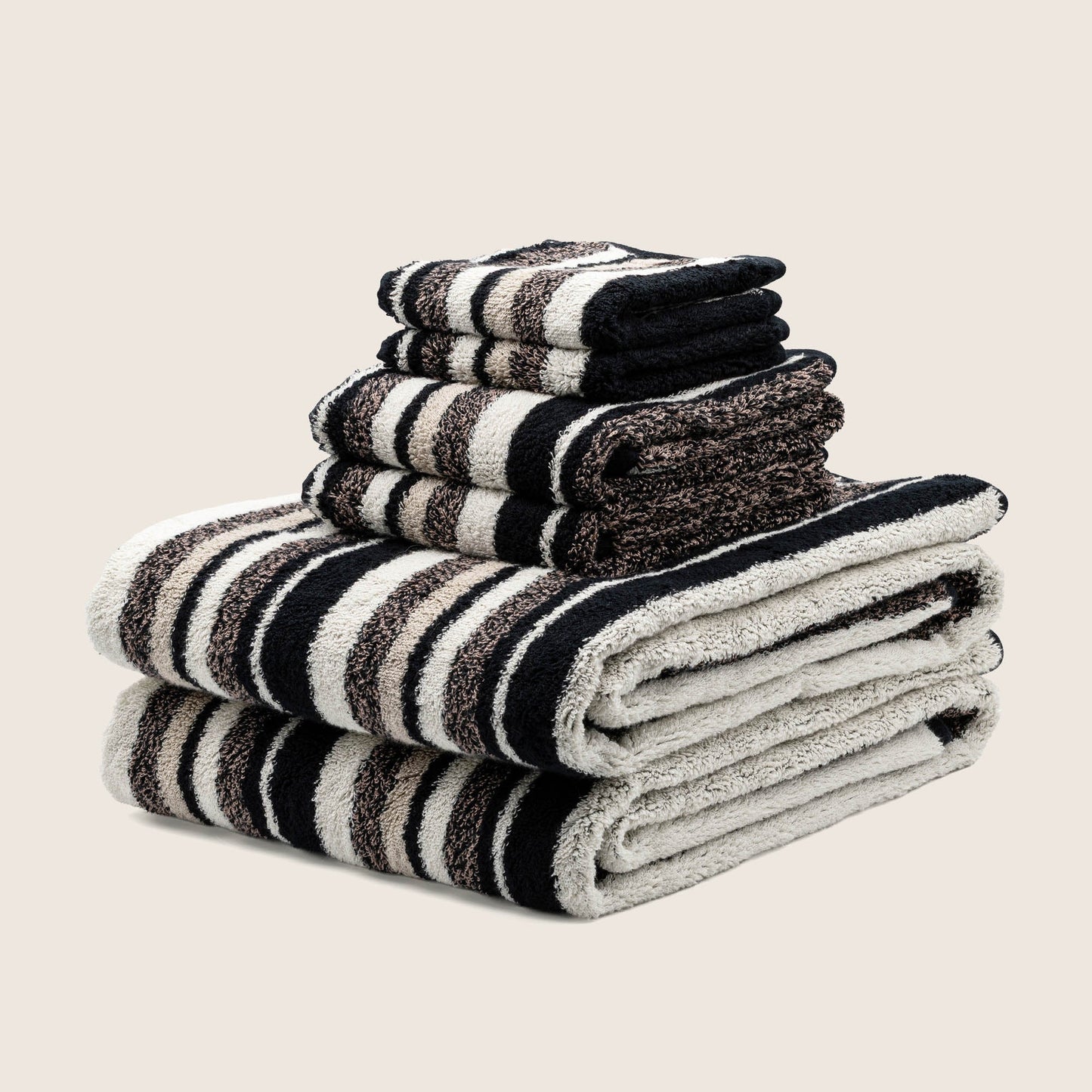 Plush striped towels stacked with dark and light bands, edges showing looped terry texture.