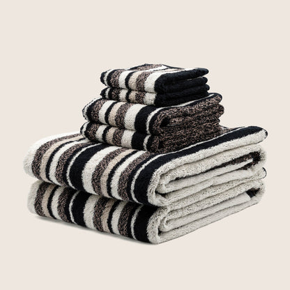 Plush striped towels stacked with dark and light bands, edges showing looped terry texture.