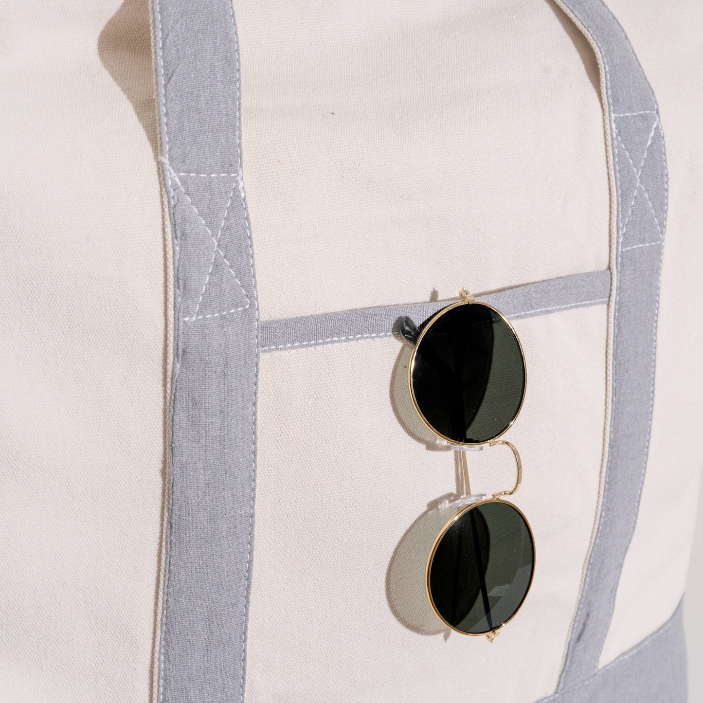 Off-white canvas tote with light gray handles and front pocket with sunglasses.