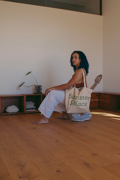 Off-white canvas tote bag with long handles and 'Summer Solace' text on front
