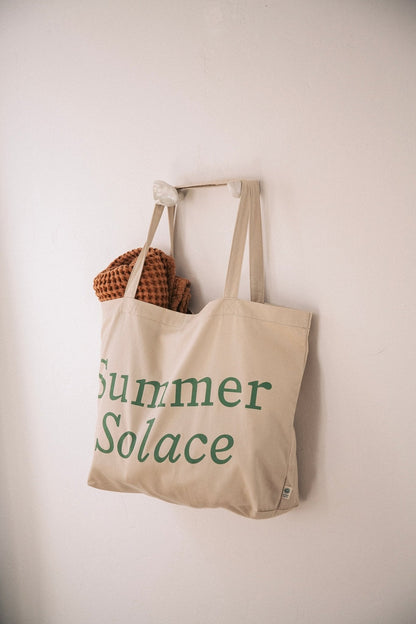 Off-white canvas tote bag with long handles and 'Summer Solace' front text