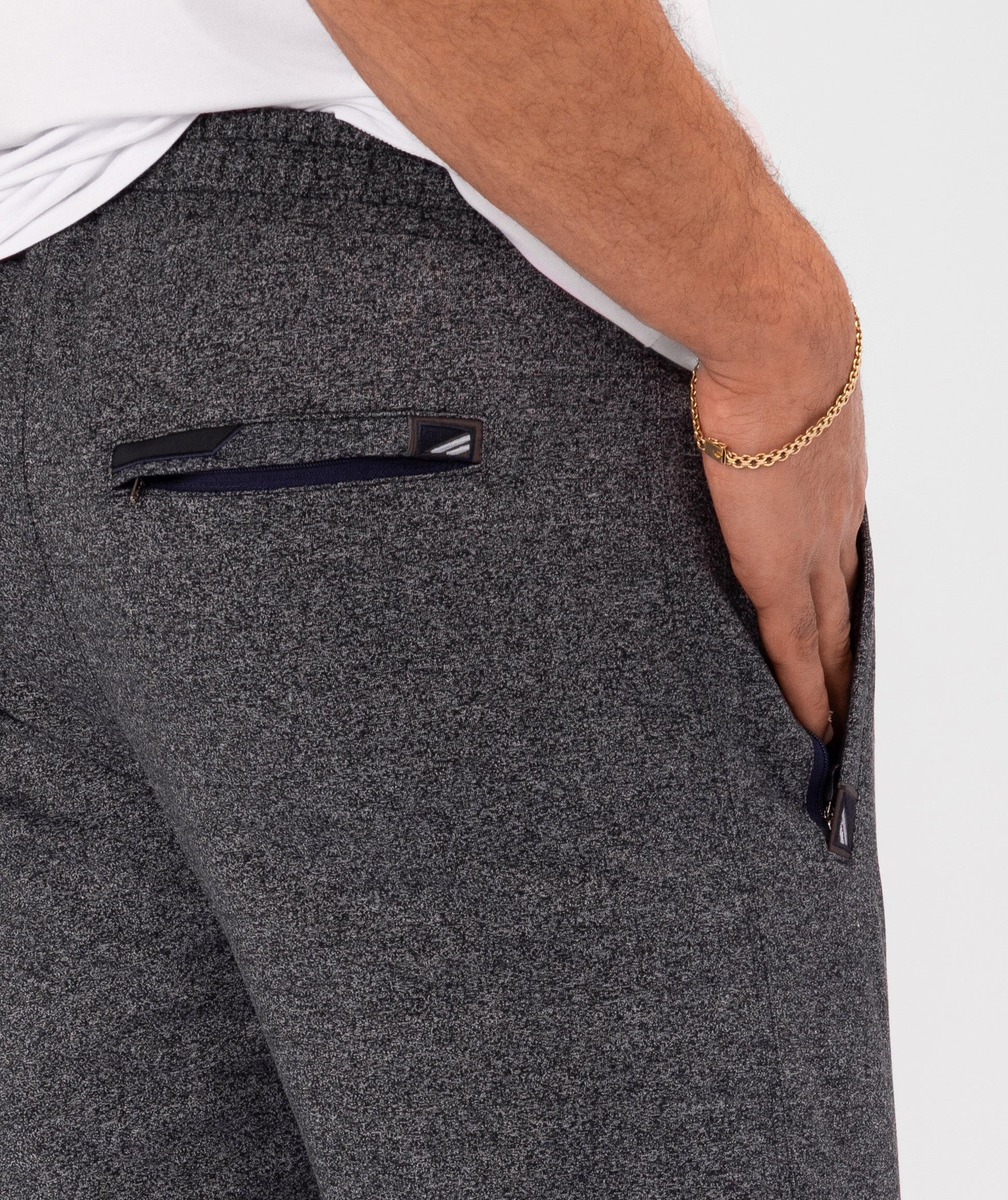Dark charcoal gray athletic sweatpants close-up: side zip pocket and stitched logo patch.