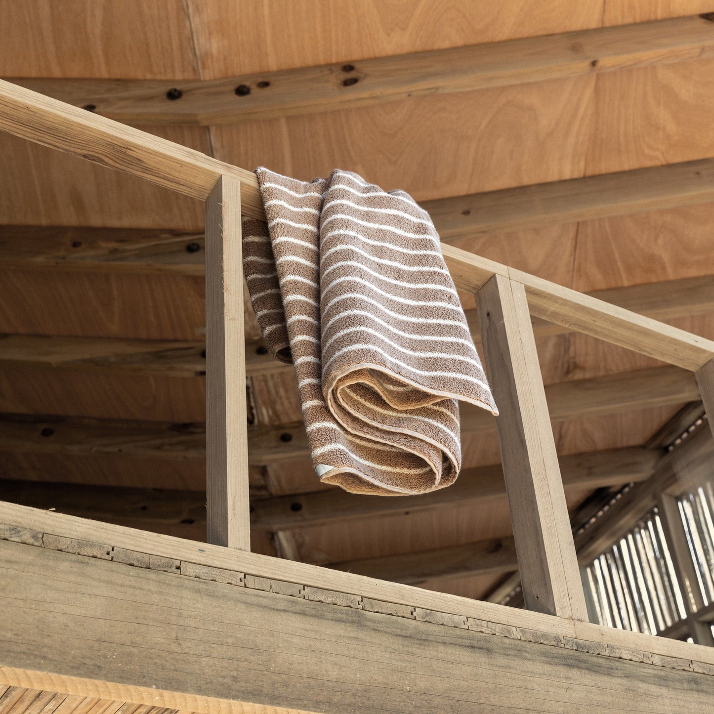 Striped towels draped on wooden loft railing, beige and white plush cotton loops
