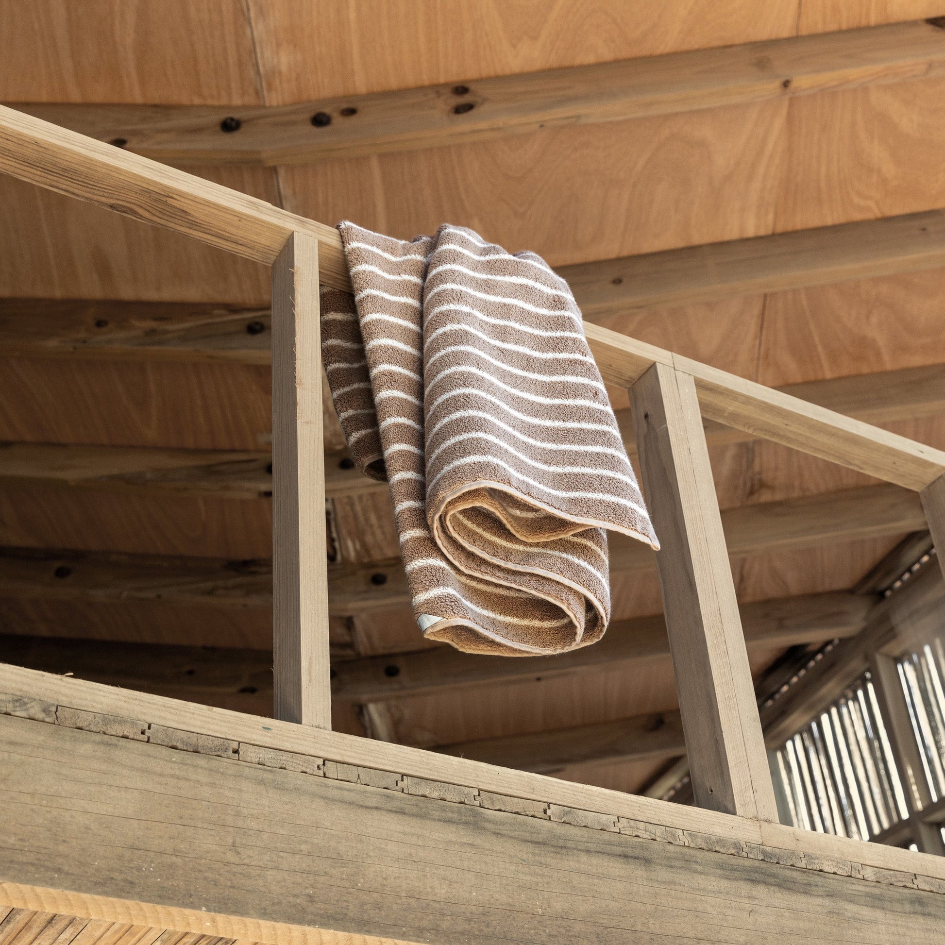 Striped towels draped on wooden loft railing, beige and white plush cotton loops