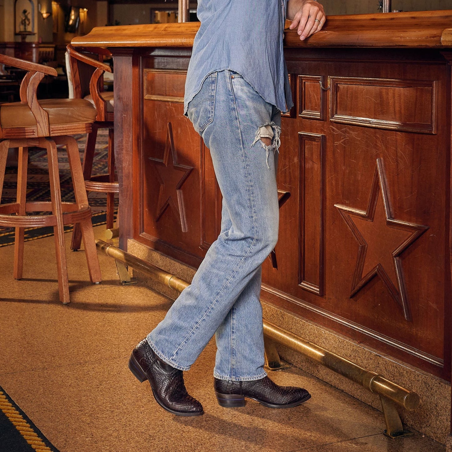 Brown cowboy boots worn with cuffed blue jeans, showing pointed toe and low heel
