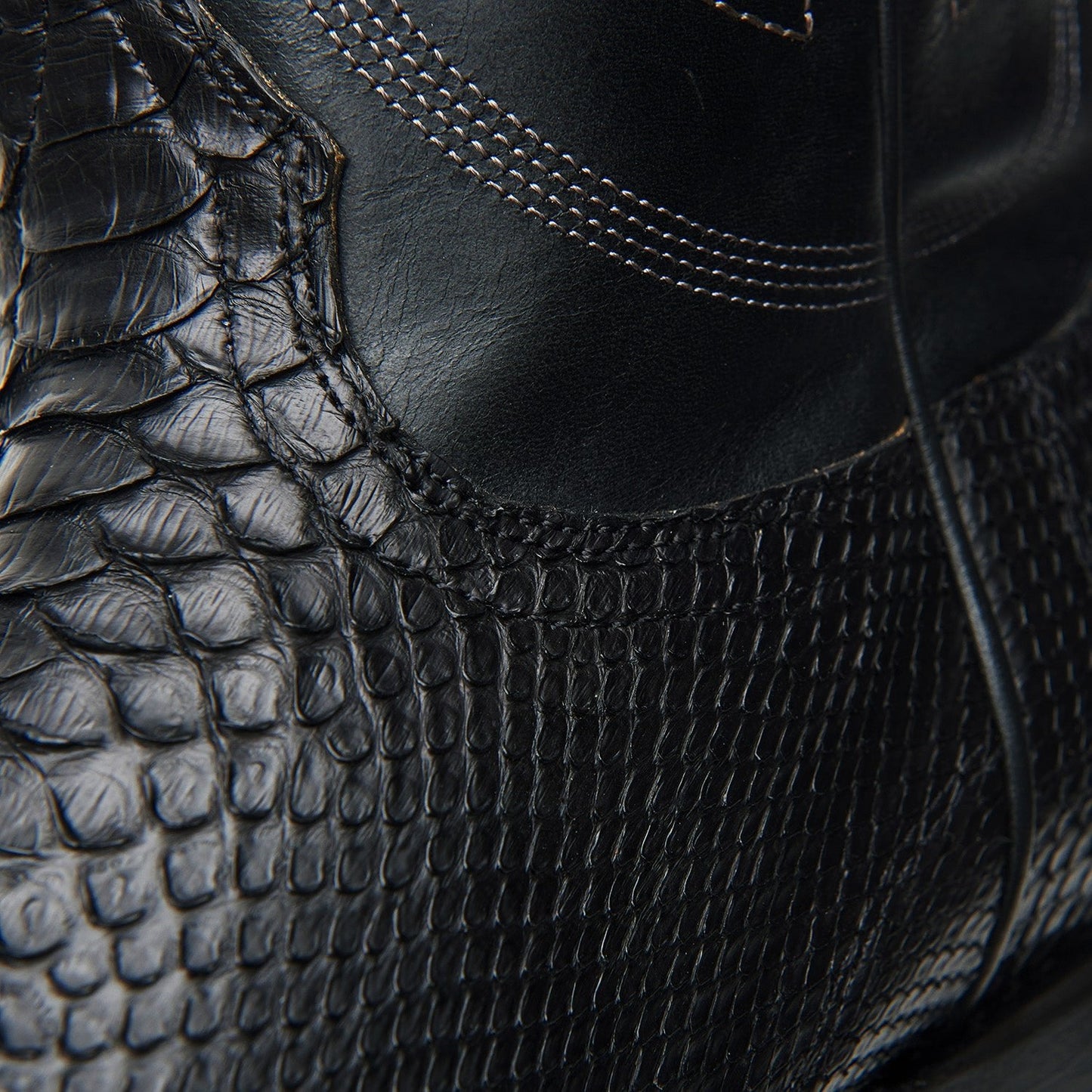 Black cowboy boot side view with crocodile-style texture and curved seam stitching
