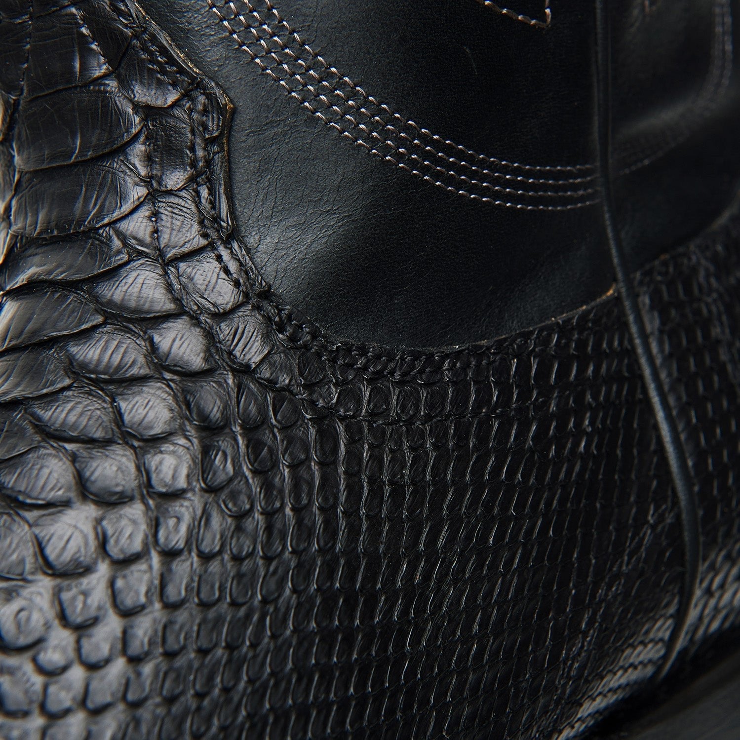 Black cowboy boot side view with crocodile-style texture and curved seam stitching