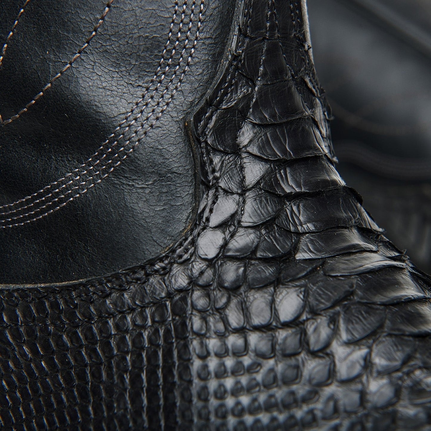 Black cowboy boot ankle close-up with crocodile texture and stitched seam detail