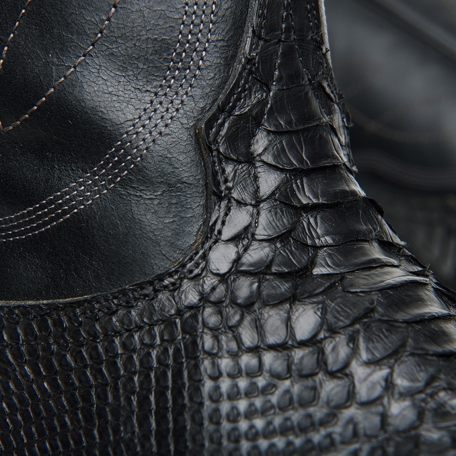 Black cowboy boot ankle close-up with crocodile texture and stitched seam detail