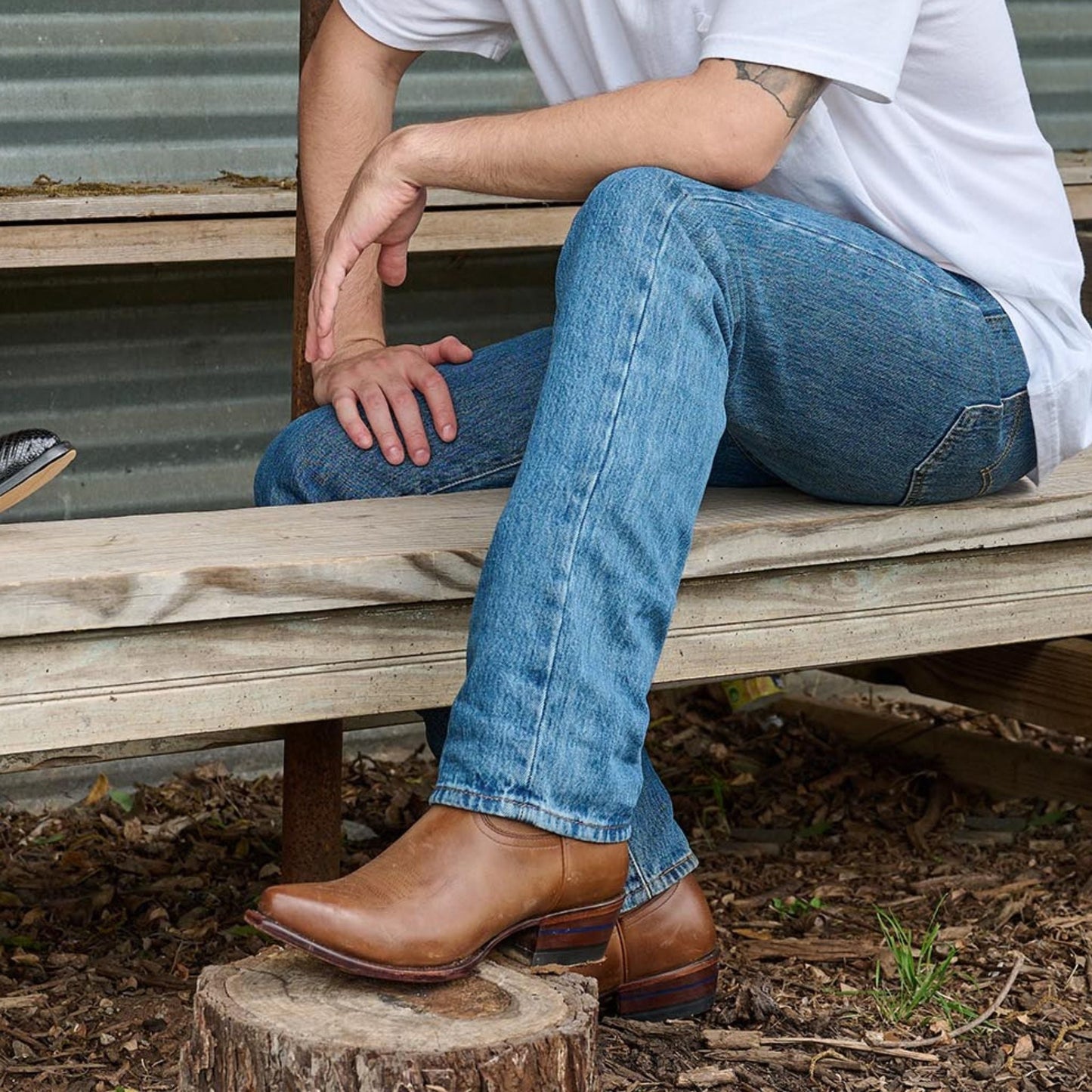 Brown cowboy boots and cuffed jeans on a wooden bench outdoors