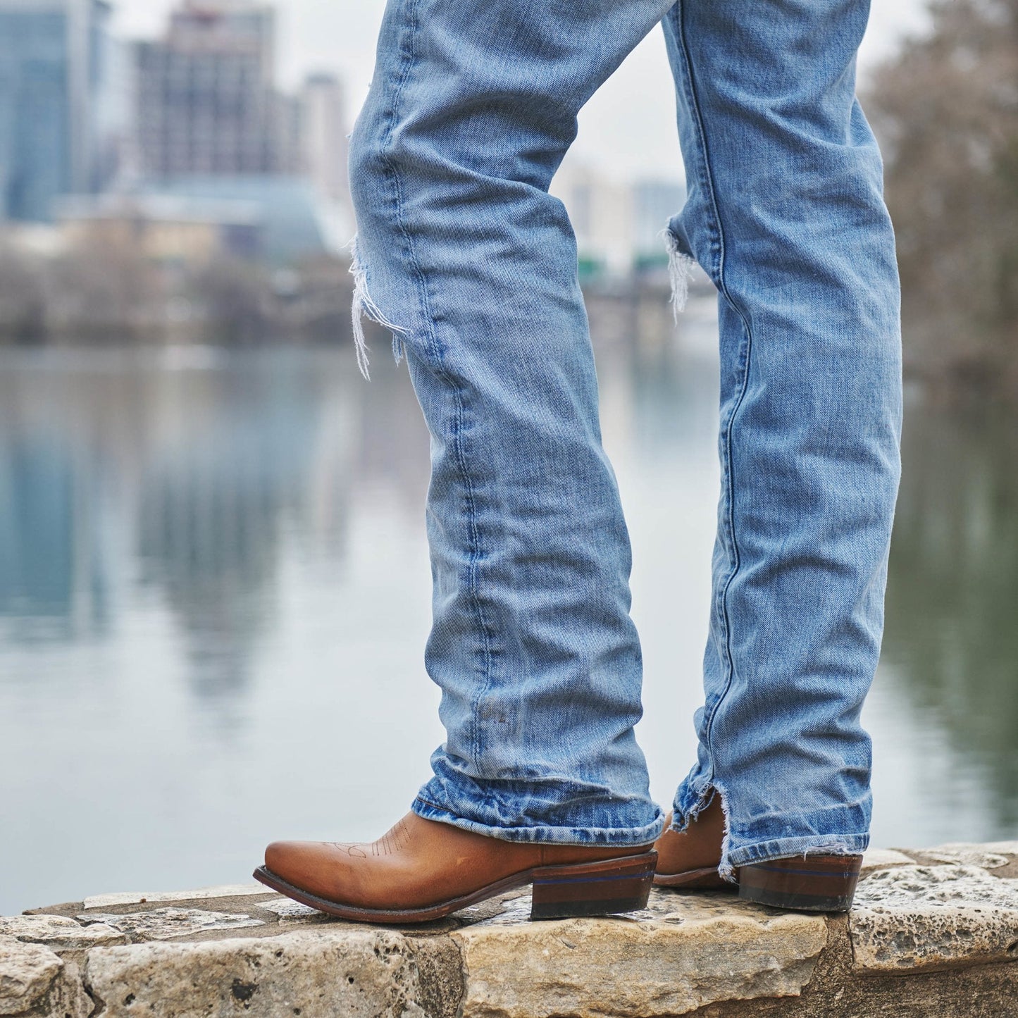 Tan cowboy boots on stone ledge with blue jeans