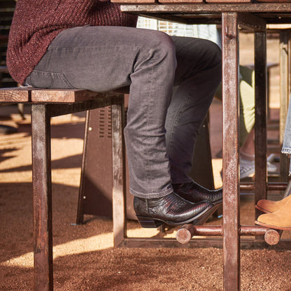The Congress cowboy boots in dark brown leather worn with gray pants on porch